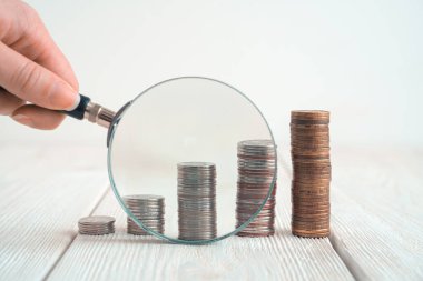 Yığınla para ve arka planda bir kadının elinde büyüteç..