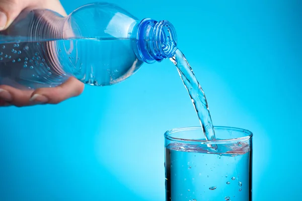 A woman pours water into a glass on a blue background.