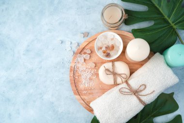 Spa ürünleri, sabun, havlu, tuz, açık mavi arka planda tropikal yapraklı mumlar..