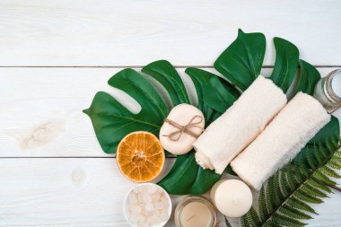 Banyo aksesuarları ve beyaz ahşap arka planda canavar yaprakları üzerinde bir dilim portakal..