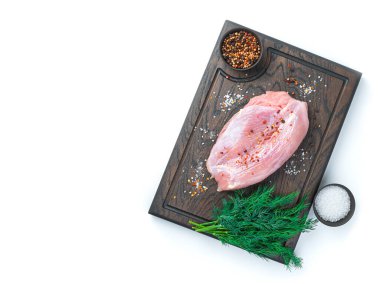 Kesme tahtasında servis edilen bir parça hindi filetosu. Beyaz arka planda yalıtılmış baharatlar ve otlar var. Üst görünüm.