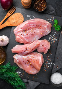 Siyah bir masada hindi fileto, tuz, baharat ve dereotu. Taze et, mutfak arka planı. Dikey yönelim.