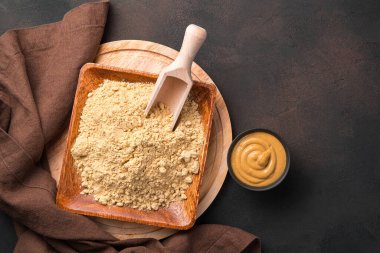 Kahverengi zemin üzerinde hardal tozu ve hazır hardal bulunan ahşap bir tabak. Kopyalamak için alanı olan mutfak arkaplanı.