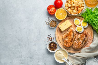 Kızarmış tavuk göğsü, yumurta, peynir, taze otlar ve gri arka planda kızarmış ekmek. Sezar salatası için malzemeler. Tarifler kavramı.