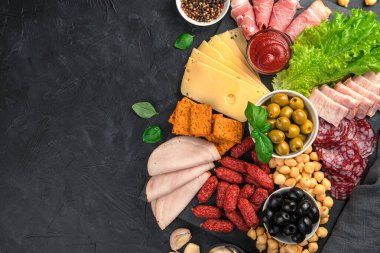 Farklı türde sosis ve peynir, siyah arka planda zeytin ve salata. Üst Manzara. Atıştırmalık konsepti.