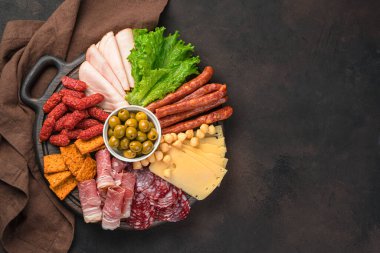 Kahverengi arka planda yuvarlak bir tahtada geniş bir sosis ve peynir çeşidi. Üst Manzara. Mutfak sosisi arka planı.