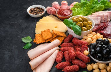 Büyük bir sosis ve peynir çeşidi siyah arka planda bir tahta üzerinde dilimlenir..