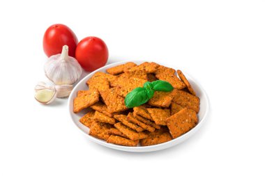 Beyaz bir tabakta domates krakerleri ve arka planda sarımsak ve domatesler, beyaz bir arka planda izole edilmiş. Doğal sağlıklı atıştırmalıklar konsepti.