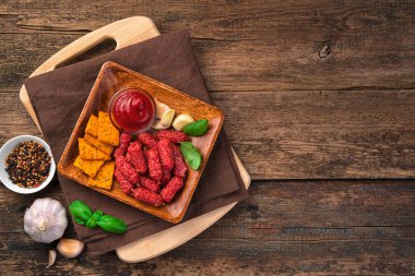 Kahverengi arka planda tuzlu atıştırmalıklar ve kopyalanacak yer. Mini sosis, domatesli İtalyan kraker ve sarımsak..