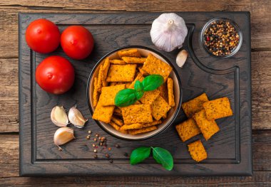 Tomato crackers with sea salt, basil and garlic on a cutting board on a brown background. Top view. The concept of Italian snacks.