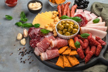 Yuvarlak masa, sosis ve peynir dilimleri, zeytin, fesleğen ve soslu koyu gri arka plan. Et lezzetleri..