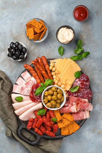 Meat cuts, sausages and cheeses of different types are cut on a board on a gray background. Charcuterie board. Top view, vertical.
