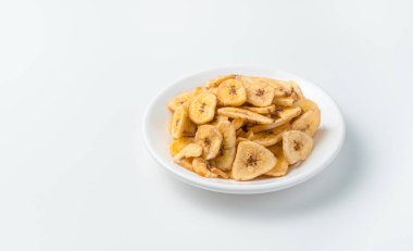 Pieces of dried bananas in a white plate on a light background. Banana chips. Side view, copy space.