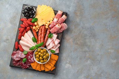 Et ve peynir aperatifi, gri arka planda zeytin ve fesleğen. Kopyalama alanı olan üst görünüm.