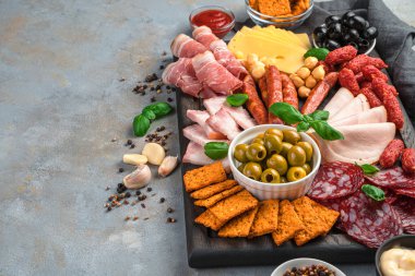 Baharat ve sarımsaklı gri bir arka planda farklı türde sosis ve peynir içeren şarküteri tahtası. Kopyalama alanı olan yan görünüm.