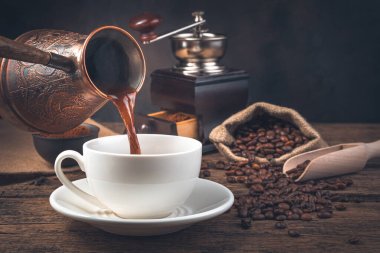 Kahve öğütücüsünün ve kahve çekirdeğinin arka planındaki bir kupa Turki 'ye kahve dökme süreci. Yan görünüm, boşluk kopyala.
