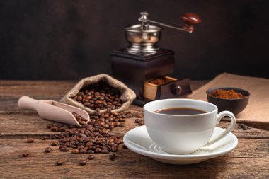 Bir fincan kahve, bir kahve öğütücü, ve kahverengi bir arka planda kopyalayacak yer olan tahıllar. Yan görünüm.