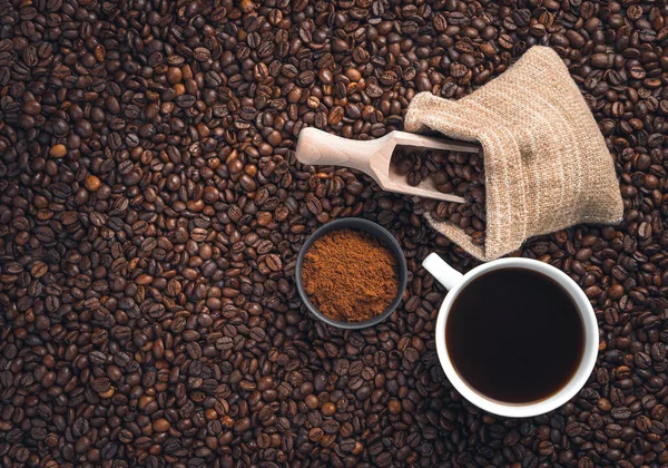 A cup of coffee, coffee beans in a bag and ground coffee on coffee beans. Top view.