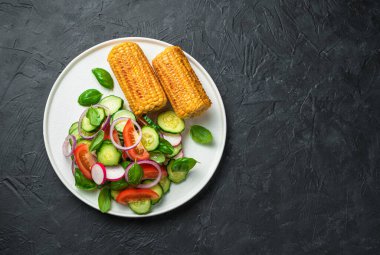 Taze sebze ve kızarmış mısır. Siyah arka planda domatesli salata, salatalık ve turp. Sağlıklı yiyecekler. Beslenme konsepti, vejetaryen yemekleri.
