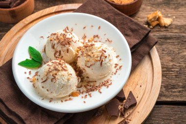 Kahverengi zemin üzerinde çikolata parçacıklı ve naneli üç top kremalı dondurma. Tatlıyı tazeliyorum. Yan görünüm.