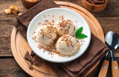 Kahverengi arka planda beyaz tabakta çikolata kırıntıları olan topların içindeki lezzetli dondurma. Yan görünüm, yakın plan.