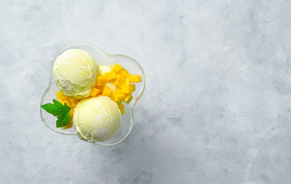 Two balls of mango ice cream and slices of fresh mango on a gray background with space to copy. Top view. Summer dessert.