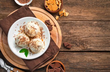 Kahverengi ahşap arka planda, üzerinde çikolata parçacıkları ve kurabiye kırıntıları olan üç top dondurma. Üst görünüm, yatay.