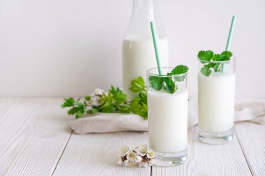 Taze mayalanmış soğuk süt, yeşil ve çiçekli beyaz arka planda iki bardak Lassi. Yan görünüm, boşluk kopyala.