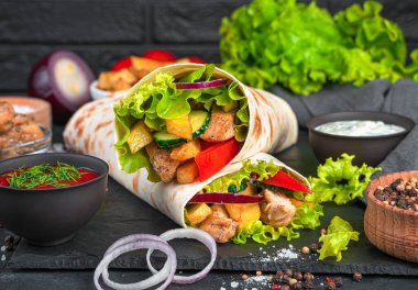 Geleneksel oryantal shawarma siyah arka planda yakın plan. Et, patates kızartması, sebze ve ekmeğe sarılmış salata. Atıştırmalık, fast food.