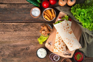 Kahverengi arka planda tavuk ve sebzeli burrito ve taze malzemeler. Fast food. Üst görünüm, alanı kopyala.