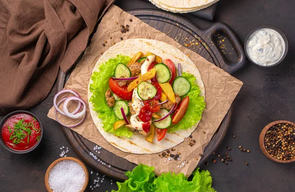 Cooking Mexican tacos on a brown background. Tortilla, meat, French fries, vegetables and hot sauce.