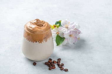 Sütlü, köpüklü kahve içeceği, kahve çekirdekleri ve gri arka planda çiçekler. Dalgona kahvesi. Yan görünüm, boşluk kopyala.