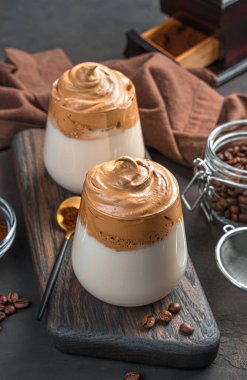 Kahverengi arka planda iki bardakta Dalgona kahvesini tazeliyorum. Yan görünüm, dikey.