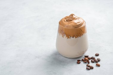 Gri arka planda Dalgona kahvesi ve kahve çekirdekleri. Yan görünüm, yakın plan.