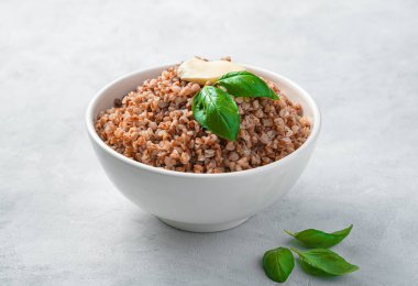 Tereyağlı karabuğday lapası ve gri arka planda taze fesleğen. Yan görünüm, yatay.