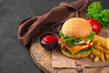 Biftek, sebze ve peynirli nefis ev yapımı burger, patates kızartması ve soslar kahverengi arka planda ve kopyalamak için yer var. Fast food.