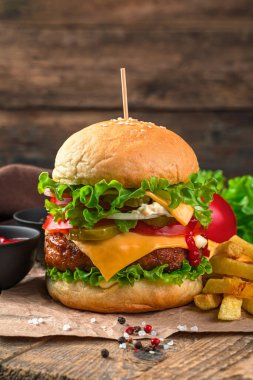 Köfteli hamburger, sebze, peynir ve kahverengi arka planda patates kızartması..
