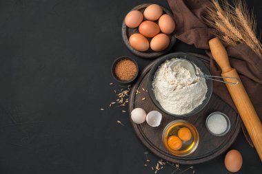 Hamurdan yemek pişirmek ve pişirmek için bir takım malzemeler. Siyah arkaplanda yumurta ve un..