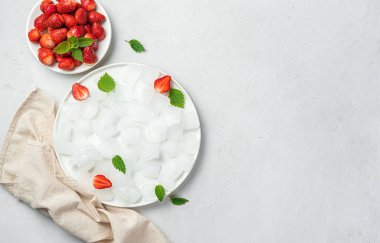 Gri arka planda nane aromalı bir tabak buz ve çilek. Üst görünüm, alanı kopyala.