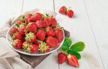 Beyaz bir tabakta, arka planda olgun çilekler. Üst görünüm, alanı kopyala.