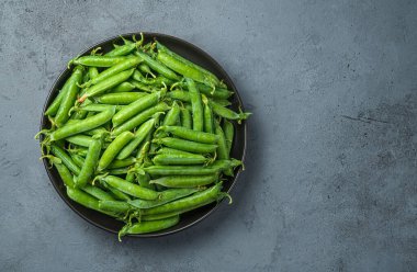 Gri arka planda bezelye kabukları olan bir tabak. Boşluğu kopyala.