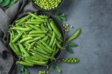 Gri arka planda siyah bir tabakta bezelye kabukları. Üst görünüm, alanı kopyala.