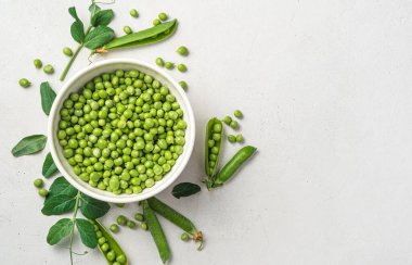 Gri arka planda beyaz kaseli yeşil bezelyeler. Üst görünüm, alanı kopyala.