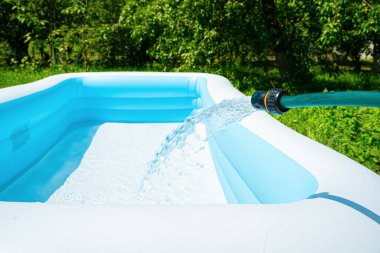 Şişirilebilir bahçe havuzu bir hortumdan gelen suyla doludur. Seçici odaklanma. Yan görünüm, kopyalamak için boşluk.