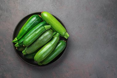 Zucchini in a black plate on a gray-brown background. Top view, copy space. clipart