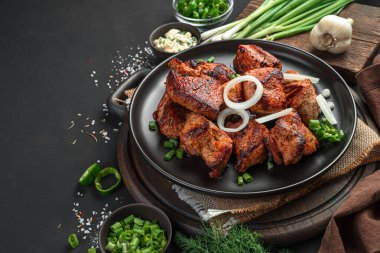 Lezzetli, soğanlı kızarmış et, siyah arka planda otlar, soslar ve baharatlar. Yan görünüm, kopyalamak için boşluk.