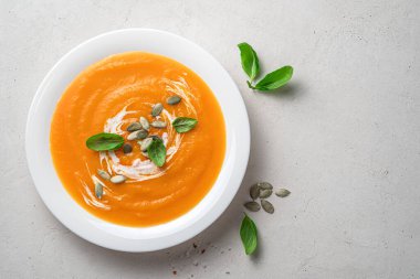 Beyaz bir tabakta beyaz bir arka planda krema ve fesleğenle kabak çorbası püresi. Üst görünüm, boşluğu kopyala. Sonbahar, vejetaryen çorbası.