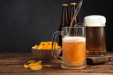 Kahverengi arka planda iki bardak bira, cips ve bira şişesi. Yan görünüm, kopyalamak için boşluk.