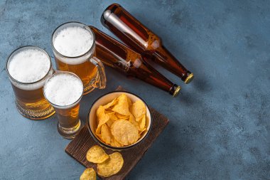 Koyu mavi arka planda bira bardakları, cips ve bira şişeleri. Yatay görünüm, kopyalamak için boşluk. Ekim Festivali.