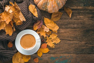 Sonbahar şenliği arka planında bir fincan kahve, yapraklar ve ahşap bir arka planda balkabağı. Üst görünüm, alanı kopyala.